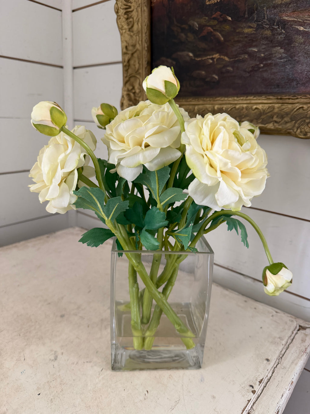 cream-colored ranunculus flower arrangement in a clear square glass vase with faux water