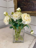 cream-colored ranunculus flower arrangement in a clear square glass vase with faux water