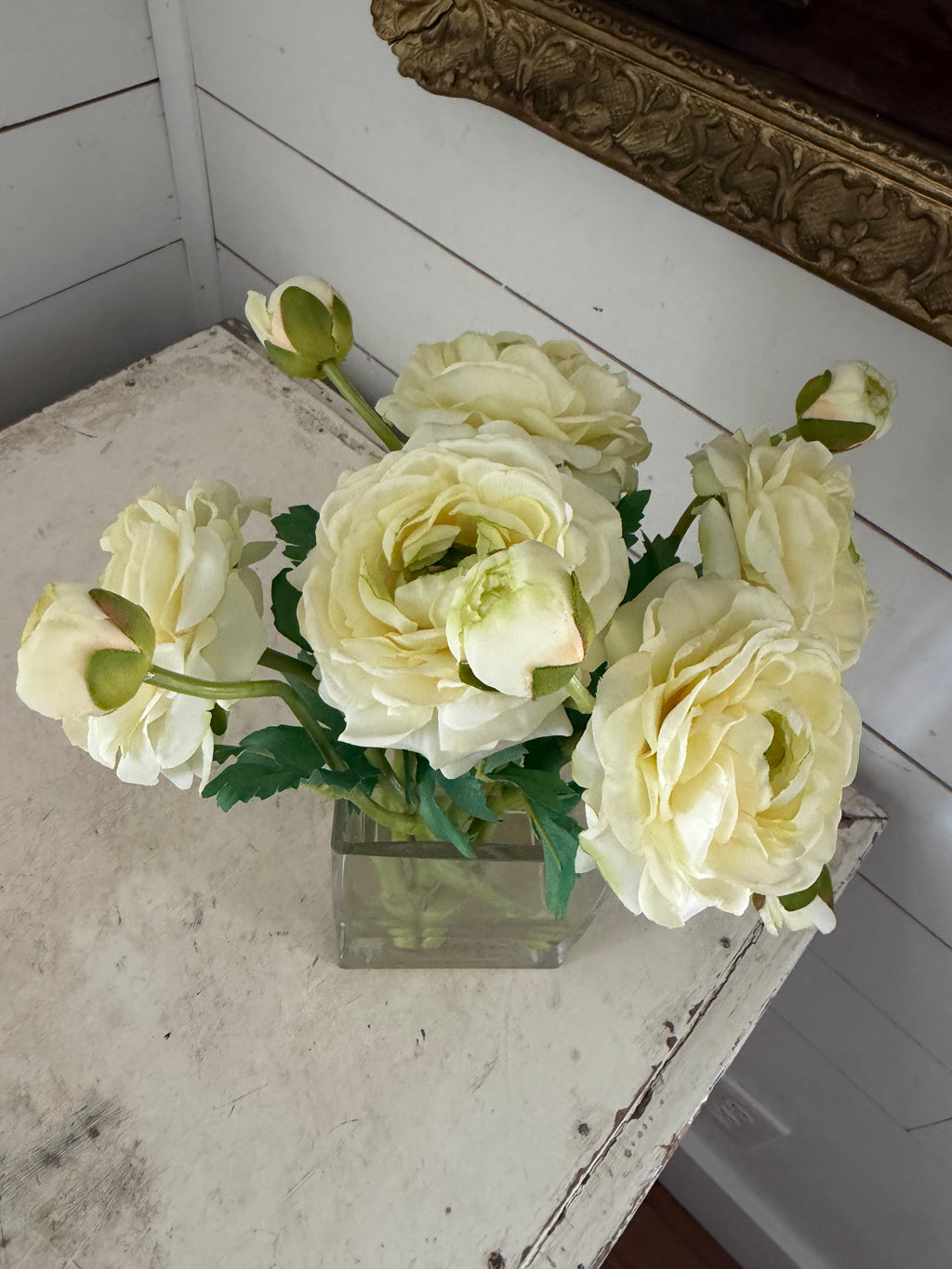 cream-colored ranunculus flower arrangement in a clear square glass vase with faux water