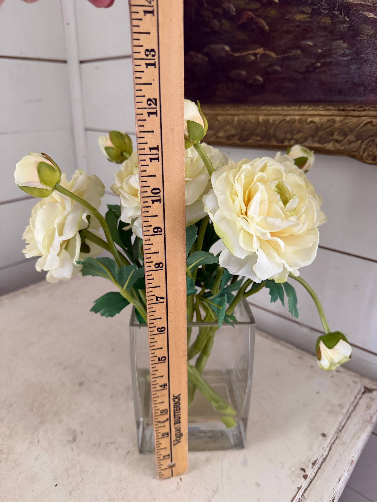 cream-colored ranunculus flower arrangement in a clear square glass vase with faux water