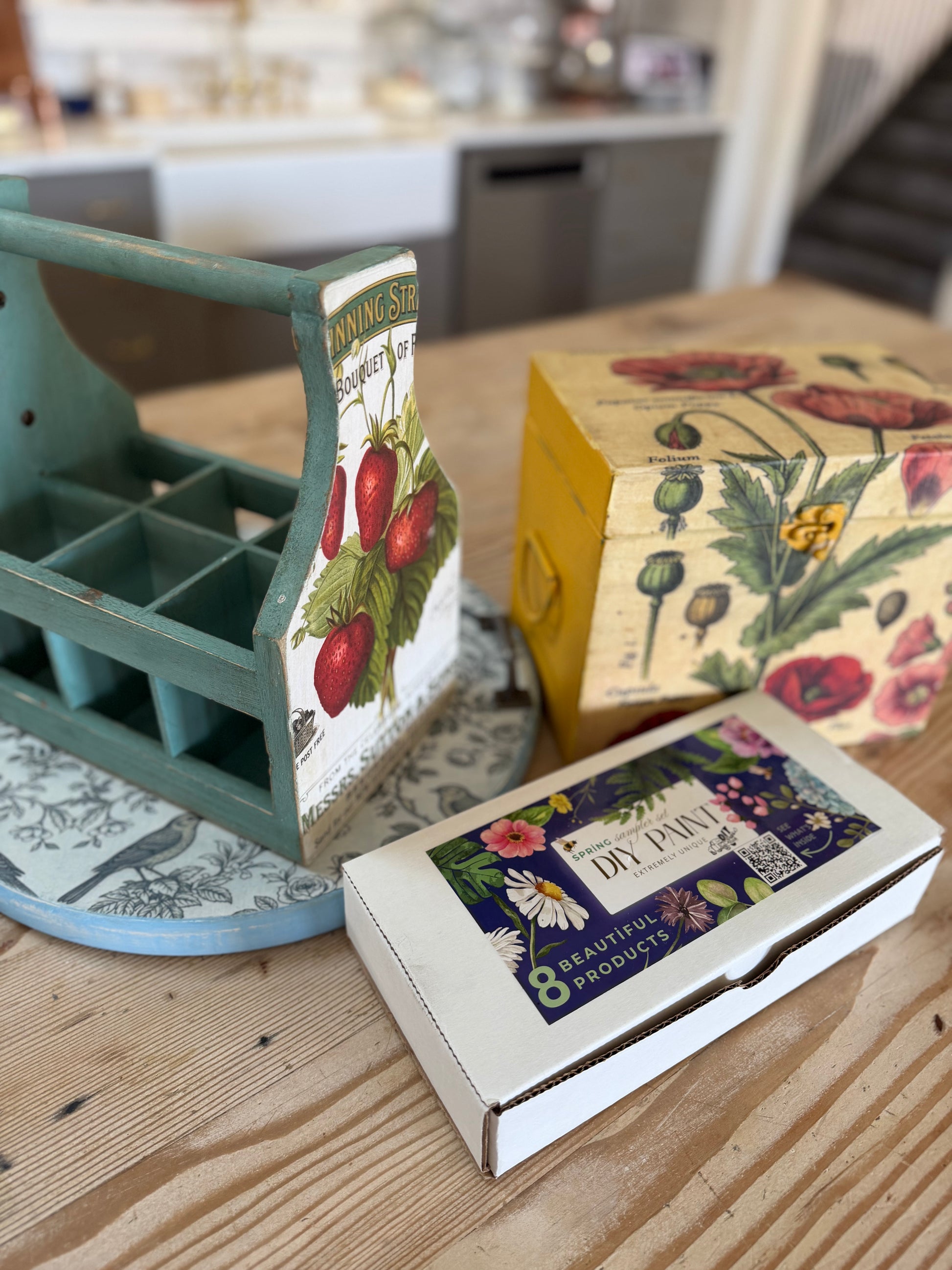 Three decorative boxes with vintage-style designs on a wooden surface. One box is labeled with the DIY Paint Mixology Kit.
