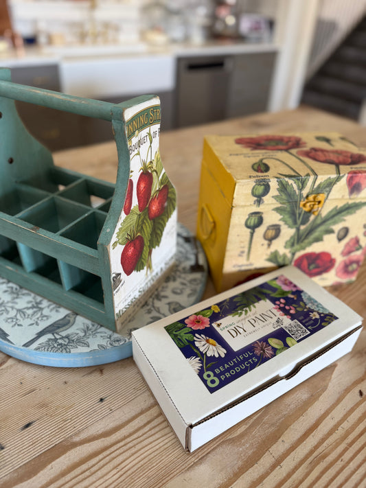 Three decorative boxes with vintage-style designs on a wooden surface. One box is labeled with the DIY Paint Mixology Kit.