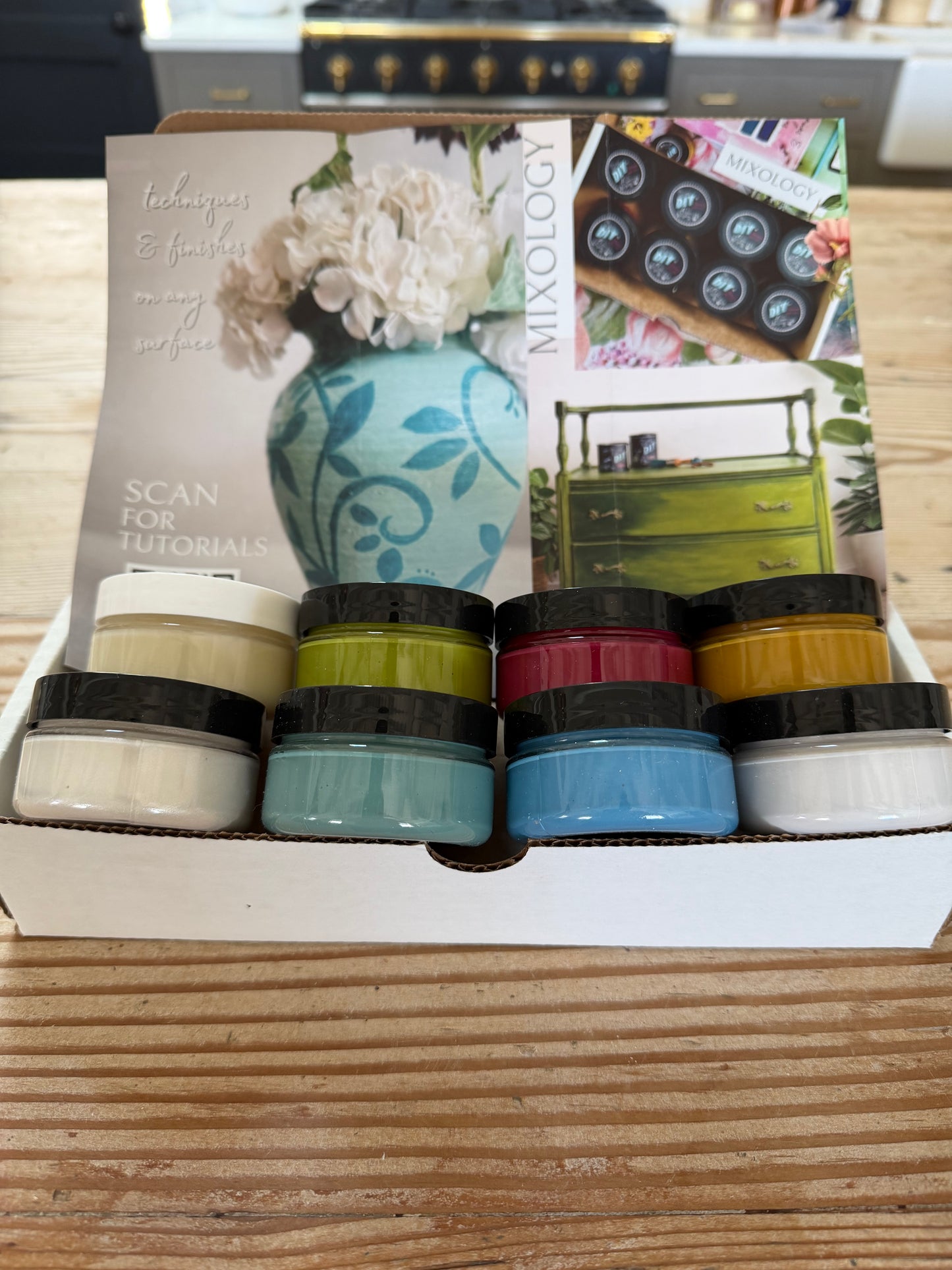 Set of 8 sample paint jars with a tutorial pamphlet on a wooden surface